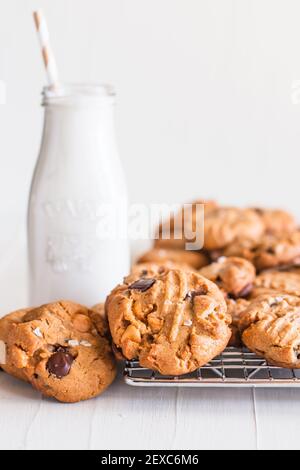 Ancora vita dei biscotti appena sfornati su un rack di raffreddamento vicino a una bottiglia di latte vecchio stile con una cannuccia in esso. Foto Stock