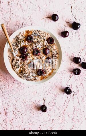 Avena notturna con ciliegie a metà e cucchiaio bianco ciotola Foto Stock