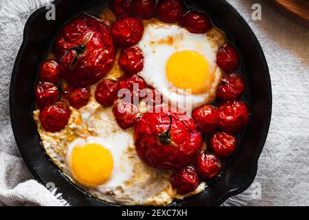 Cuocere i pomodori arrostiti e le uova con il lato soleggiato in un padella in ghisa Foto Stock