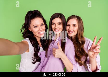 Ritratto fotografico di ragazze che sorridono sorrise prendendo selfie mostrando come gesti v-sign isolati su uno sfondo di colore verde intenso Foto Stock