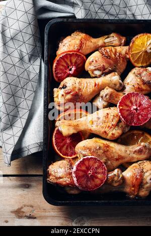 Bastone di pollo arrosto con spezie in padella. Cosce di pollo al forno con arance. Foto Stock