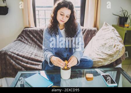 giovane donna con biscotti e caffè a colazione seduta su il divano Foto Stock