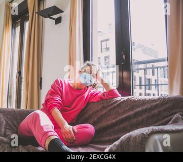 giovane donna con maschera protettiva sul divano Foto Stock