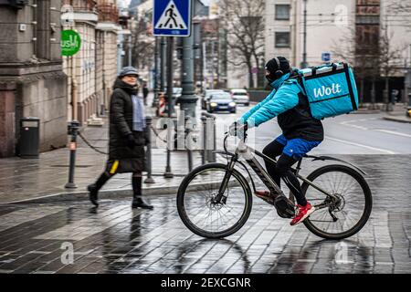 Rider con bici e maschera sotto la pioggia che lavora per Wolt, servizio online di ordinazione e consegna di cibo che prende gli ordini tramite un'app mobile Foto Stock