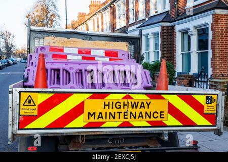 Cartello Dayglo "manutenzione dell'autostrada" sul retro di un autocarro che trasporta coni stradali arancioni e sezioni di recinzione in plastica viola, Londra, Regno Unito Foto Stock