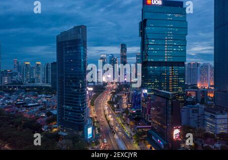 Vista aerea dell'autostrada a più corsie attraverso il moderno centro della città con grattacieli alti in luce blu notturna traffico notturno attraverso il centro di Giacarta, Indonesia Foto Stock