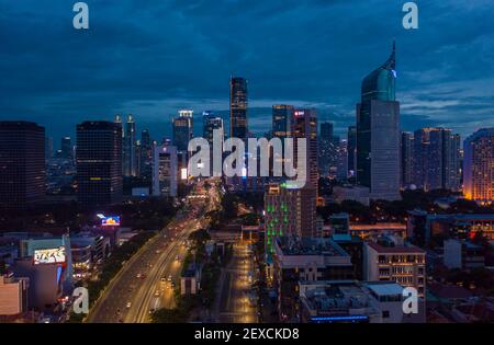 Vista aerea notturna dei grattacieli e dell'autostrada a più corsie nel grande paesaggio urbano del centro cittadino degli alti edifici di Giacarta, Indonesia di notte Foto Stock