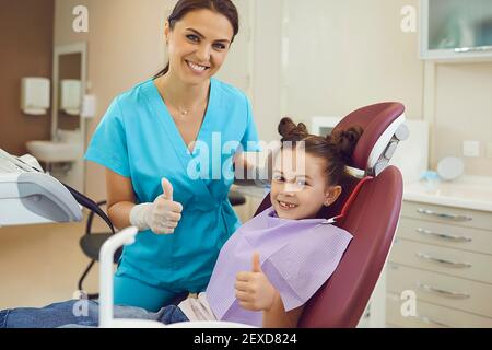 Donna dentista e paziente ragazza mostrando pollici su segno e. sorridente durante l'esame dei denti in studio dentistico Foto Stock