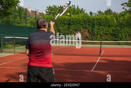 Pensionati che giocano a tennis all'aperto sul campo da tennis in terra battuta, anziani attivi, concetto sportivo Foto Stock