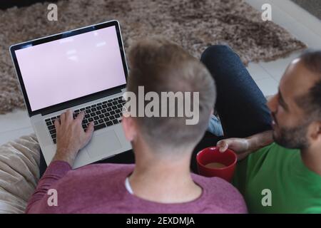 Multi etnico gay maschio coppia seduta sul divano utilizzando il computer portatile con spazio per la copia sullo schermo a casa Foto Stock