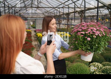 Instagram fotografo blogging workshop concetto. Primo piano le mani delle donne che tengono il telefono e scattano foto della ragazza con i fiori. Messa a fuoco selettiva. Foto Stock