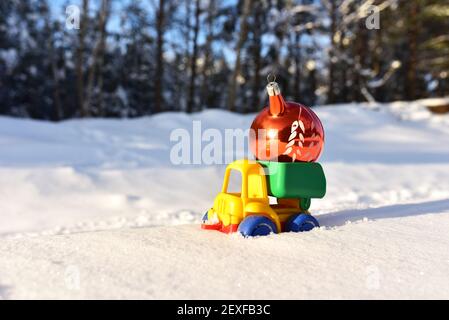 Camion giocattolo con una palla di Natale sullo sfondo di neve bianca nella foresta. Сoncept di prepararsi per la celebrazione del nuovo anno. Regali di shopping, decoratin Foto Stock