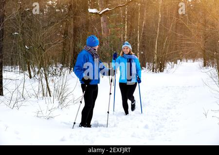 Coppia anziana che cammina con bastoni nordici in inverno innevato parcheggio Foto Stock