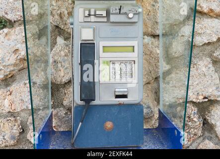 Foto ravvicinata di un vecchio telefono pubblico a gettoni e carte posto su un muro roccioso a Frigiliana, Malaga, Spagna Foto Stock