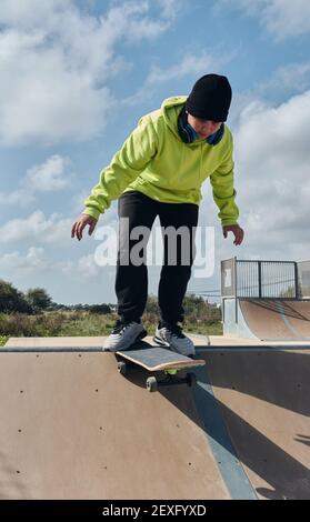 giovane, adolescente, con skateboard, immersioni in discesa, su una pista, skateboard, indossare cuffie, felpa verde, cappello nero, oscillante, su a s. Foto Stock