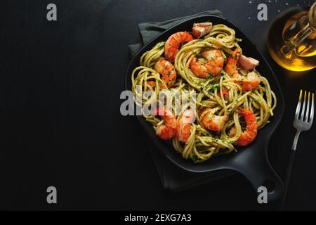 Gustosa pasta appetitosa con gamberi e salsa pesto servita su una padella scura. Vista dall'alto. Foto Stock