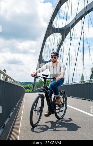 Il ciclista in bicicletta elettrica attraversa l'East Harbour Bridge a Francoforte sul meno, Hessen, Germania. Foto Stock