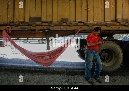 Caracas, Venezuela. 04 marzo 2021. Il conducente di un camion, che collega i lunghi tempi di attesa di fronte alla stazione di servizio nella sua amaca, si trova accanto all'auto sul lato di una strada di campagna e guarda nel suo cellulare. A causa della mancanza di carburante, i carrelli a volte si accodano per ore davanti alle stazioni di servizio. La benzina è ripetutamente in approvvigionamento corto nel paese con le riserve di petrolio più grandi del mondo. Alla fine del 2020, diversi carichi di carburante in autocisterna erano stati consegnati in Venezuela dall'Iran. Credit: Jesus Vargas/dpa/Alamy Live News Foto Stock