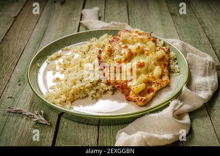 pollo alla griglia con ananas e formaggio con riso in un elegante piatto di porcellana verde, sul vecchio tavolo di legno verde Foto Stock