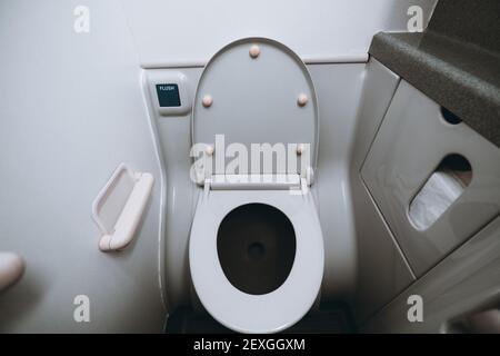 Vista grandangolare di una parte dell'interno e di un recipiente per wc con il coperchio aperto all'interno di un piccolo toilette a bordo di un aereo passeggeri in pla grigio Foto Stock