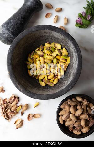 Pistacchi sbucciati nel mortaio di marmo nero su fondo di marmo bianco. Foto Stock