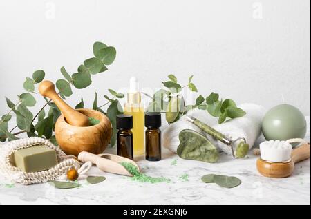 Cura naturale della pelle e aromaterapia con bottiglie di olio essenziale di eucalipto, sale da bagno, rullo di giada di bellezza, gua sha su marmo. Spa, benessere, massaggi e. Foto Stock