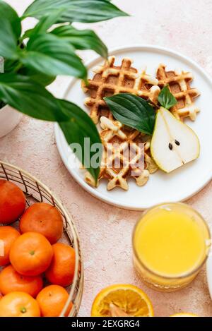 waffle fatti in casa su sfondo rosa chiaro. succo d'arancia. frutta Foto Stock