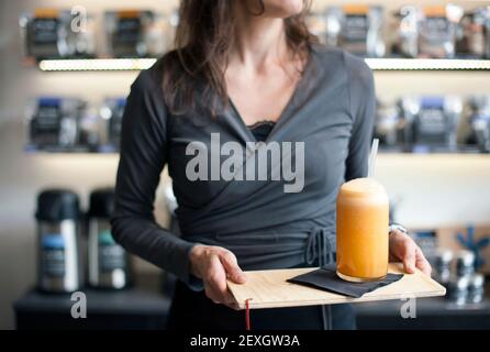 Primo piano di servizio cameriera, mani che tengono un bicchiere di succo d'arancia su vassoio sano stile di vita concetto Foto Stock