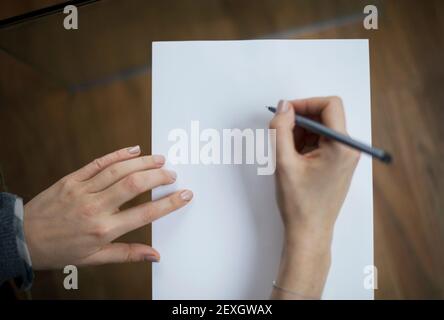 Mano femmina che tiene una penna, iniziando a scrivere su un foglio bianco vuoto di carta A4 con spazio per la copia. Prendere nota del concetto di processo di creazione, disegno o scrittura Foto Stock