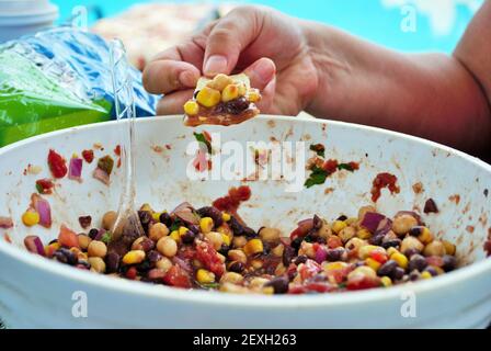 immergere a mano il chip di tortilla in fagioli neri freschi e mais insalata in una grande ciotola da portata Foto Stock