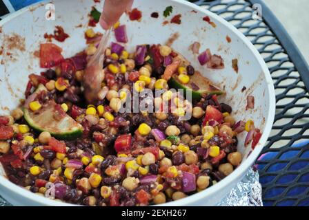 mescolare a mano fagioli neri freschi e insalata di mais in un ampia ciotola da portata Foto Stock