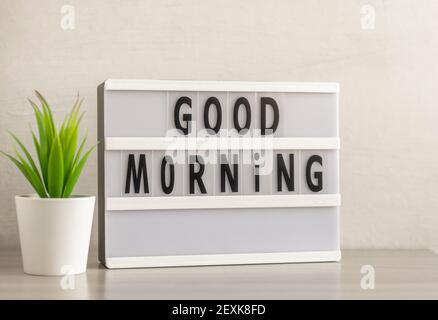 Buongiorno è scritto su una scatola luminosa sul tavolo accanto al fiore. Foto Stock