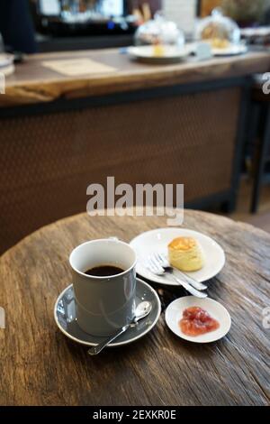 Una tazza di caffè nero caldo in ceramica servita con burro cono semplice e confettura di bacche su tavolo di legno Foto Stock