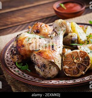 Cosce di pollo al forno con patate a fette ed erbe. Bastoncini di pollo al barbecue su un tavolo di legno. Foto Stock