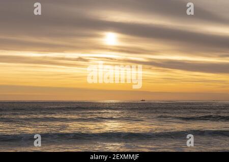 Una vista affascinante dell'oceano ondulato che brilla sotto tramonto che si inforia attraverso il cielo nuvoloso Foto Stock