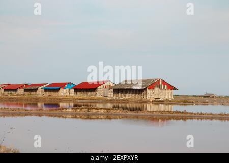 Una vista dei campi di sale con legno deposito case di sale sullo sfondo a Kampot, Cambogia Foto Stock