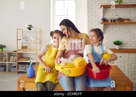 Madre sorridente e due figlie sedute a tavola con la famiglia per la pulizia della casa Foto Stock