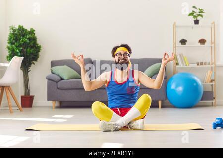 Divertente uomo felice in abbigliamento sportivo retrò seduto in yoga facile posa e imparare a meditare Foto Stock