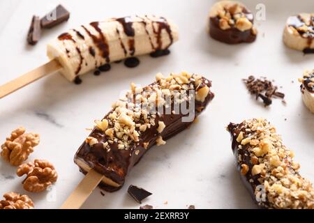 Lecca di banana surgelata o lecci con noci spruzzare per i bambini su bianco. Dolci vegani fatti in casa. Primo piano. Foto Stock
