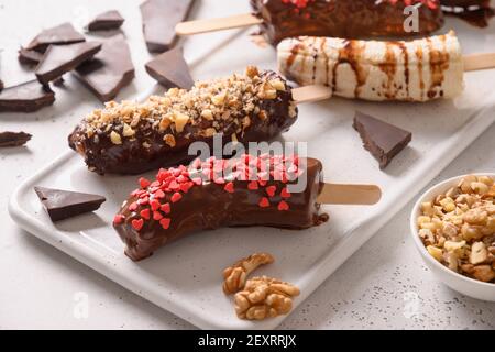 Lecca di banana surgelata o lecci con noci spruzzare per i bambini su bianco. Dolci vegani fatti in casa. Primo piano. Foto Stock