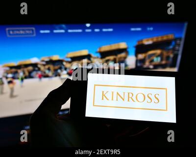 Persona che detiene smartphone con il logo della società mineraria canadese Kinross Gold Corporation sullo schermo davanti al sito Web. Mettere a fuoco il display del telefono. Foto Stock