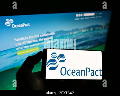 Persona che detiene il cellulare con il logo della società brasiliana OceanPACT Serviços Marítimos S.A. sullo schermo davanti alla pagina web. Mettere a fuoco il display del telefono. Foto Stock