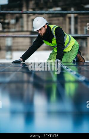 Operatore che monta pannelli solari sul tetto degli uffici del City Council di Edimburgo, Waverley Court, Edimburgo, UK. Foto Stock