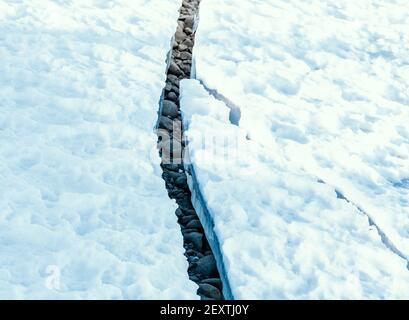 Grande crepa in ghiaccio permafrost rivelando rocce asciutte nascoste sotto. Foto Stock