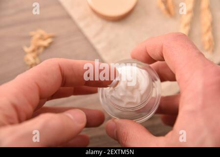 Mani che prendono crema idratante naturale di estratto di avena per l'applicazione con tavolo in legno con vista dall'alto con punte di avena Foto Stock