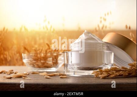 Crema idratante naturale con estratto di avena in vaso di vetro tavola in legno in campo di punte di avena con sfondo sole Foto Stock