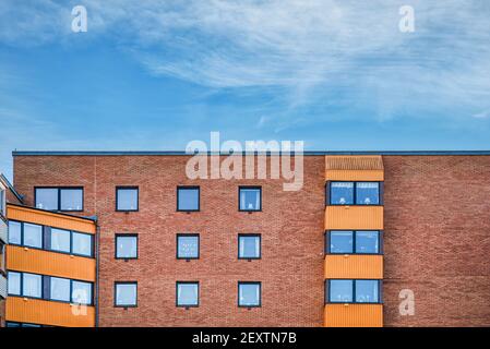 Parete in mattoni parte superiore di una facciata contemporanea. L'edificio si compone di moderni appartamenti che presentano un esterno fatto di mattoni di fuoco arancioni Foto Stock