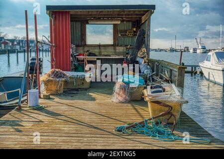 Un'ancora arrugginita con una corda blu chiaro legata su un molo di legno. Capanna di pescatori con molti attrezzi da pesca in un villaggio di pescatori o porto di pescatori Foto Stock