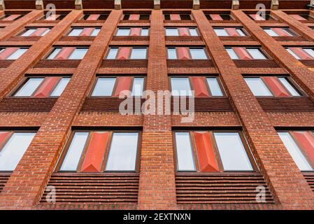 Moderno edificio residenziale con una facciata in mattoni arancioni. Ripetizione delle finestre o motivo delle finestre su un esterno coperto di mattone arancione Foto Stock