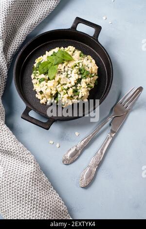 Risotto con foglie di spinaci giovani arrangiate in ghisa piatto nero con coltello e forchetta Foto Stock